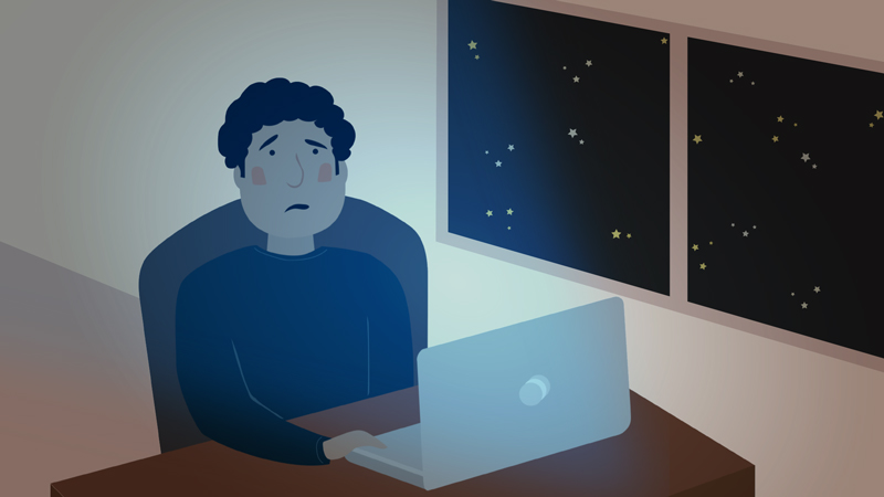 A man sitting in a dark room, staring blankly at a laptop screen.